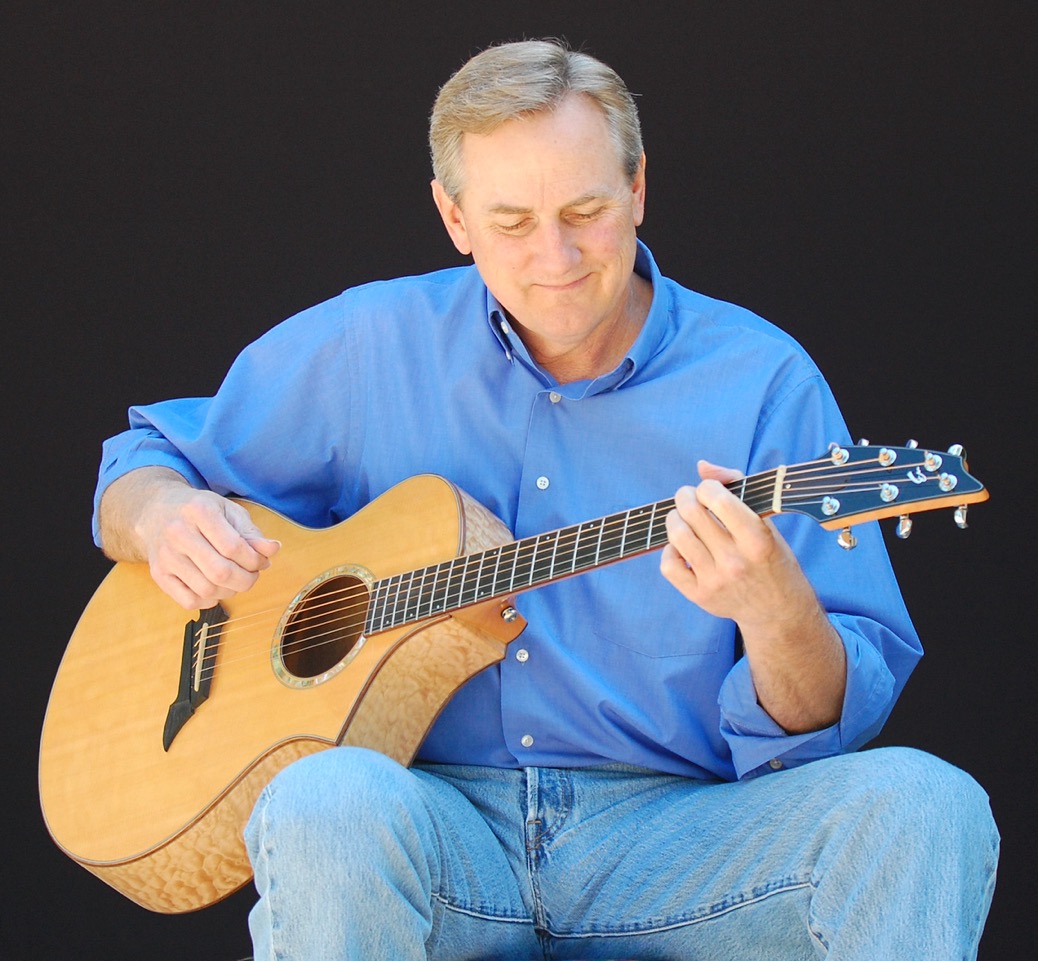 Kyle Freeman seated and looking down while playing his acoustic guitar