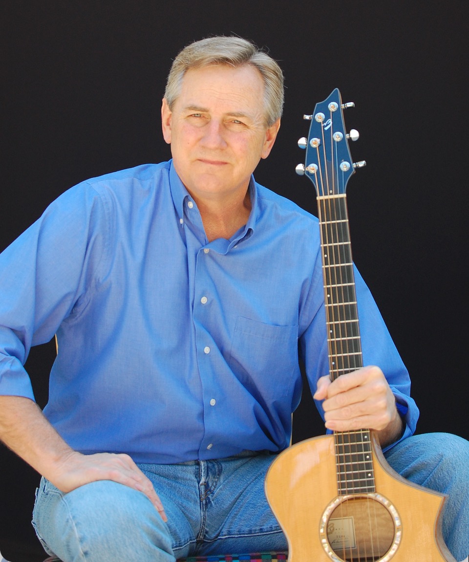 Kyle Freeman seated with his acoustic guitar against a dark backdrop